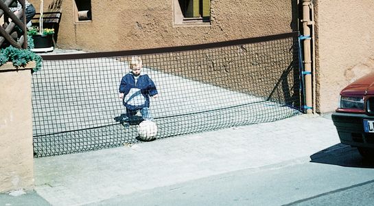 Absperrnetz, zwischen Hauswand und Mauer mit Kind und Ball hinter dem Netze, mit einem Auto kommend