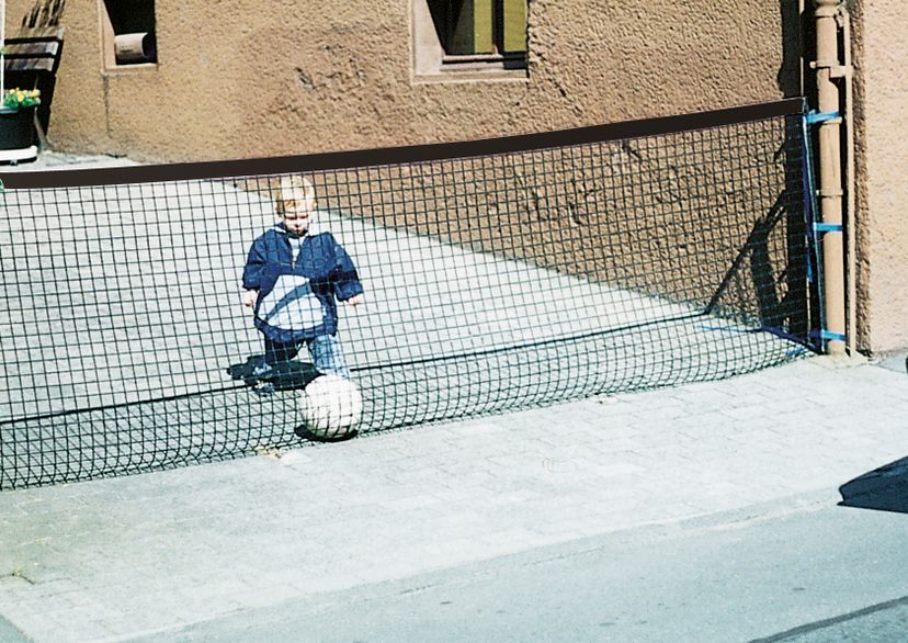 Absperrnetz, zwischen Hauswand und Mauer mit Kind und Ball hinter dem Netze, mit einem Auto kommend